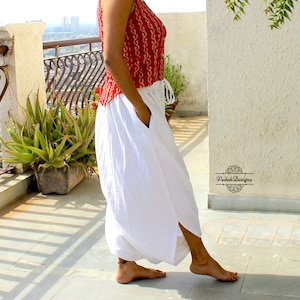 May include: A sleeveless red top with a white repeating pattern paired with loose white trousers featuring a drawstring waist and side pockets. The trousers have a split hem design. The text Vedah Designs is printed on the wall in black.