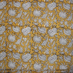 May include: A mustard yellow fabric featuring a repeating pattern of white floral and leaf motifs outlined in thin black lines. The design consists of stylized blossoms and foliage arranged in a dense, continuous botanical print across the surface.