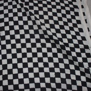 May include: A piece of fabric featuring a repeating black and white checkered pattern. The design consists of uniform square shapes arranged in a grid, with the black squares showing slight variations in their edges and texture across the surface.