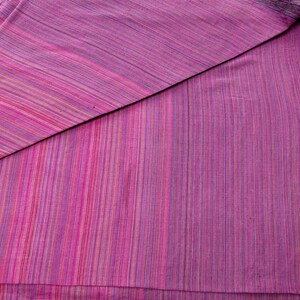Puede incluir: Un trozo de tela doblado con un patr&oacute;n de rayas en tonos de rosa, morado y blanco.