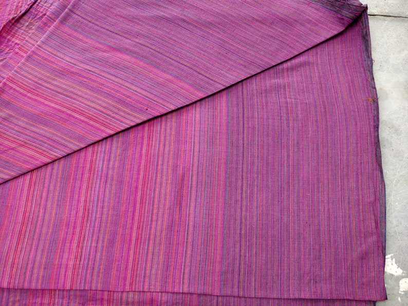 Puede incluir: Un trozo de tela doblado con un patr&oacute;n de rayas en tonos de rosa, morado y blanco.