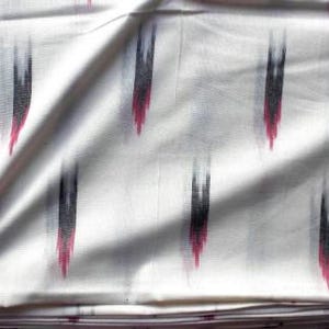 May include: A white fabric featuring a repeating ikat pattern of vertical, blurred brushstroke-like shapes in black and magenta. The textile has a smooth, woven appearance with soft folds that create subtle shadows across the surface of the material.