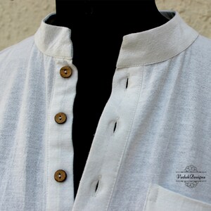 May include: White cotton shirt with a mandarin collar and wooden buttons. The shirt has a pocket on the left side and the text "Vedah Designs" is printed on the bottom right corner.