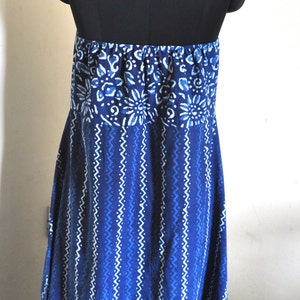 May include: A blue and white patterned halter dress on a black mannequin. The dress features a floral design at the top and a zig-zag pattern on the skirt. The halter tie is adorned with small gold beads.