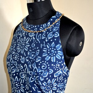 May include: A sleeveless, indigo blue dress with a white floral pattern is displayed on a black mannequin. The dress has a beaded neckline and a fitted bodice. The dress is a halter style and is made of a soft fabric. The dress is a summer dress.