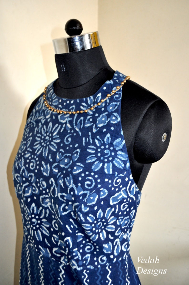 May include: A sleeveless, indigo blue dress with a white floral pattern is displayed on a black mannequin. The dress has a beaded neckline and a fitted bodice. The dress is a halter style and is made of a soft fabric. The dress is a summer dress.
