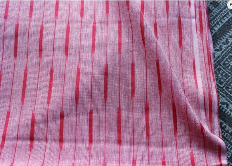 May include: A piece of woven fabric featuring a light pink base with a repeating pattern of vertical red stripes. The stripes are composed of elongated, dashed segments that create a textured appearance across the surface of the textile material.