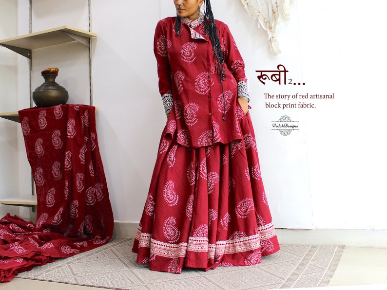May include: A woman wears a red and white paisley print top and skirt. The top has a collar and long sleeves. The skirt is long and flowing. The text "खबी... The story of red artisanal block print fabric." is visible in the image.