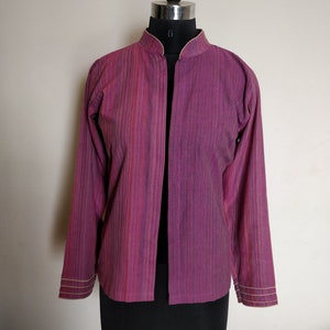 Puede incluir: Una chaqueta de manga larga, abierta por delante, con cuello mandar&iacute;n. La chaqueta est&aacute; hecha de una tela a rayas en tonos rosa, morado y blanco. Los pu&ntilde;os y el cuello est&aacute;n ribeteados con una fina tela de color crema.