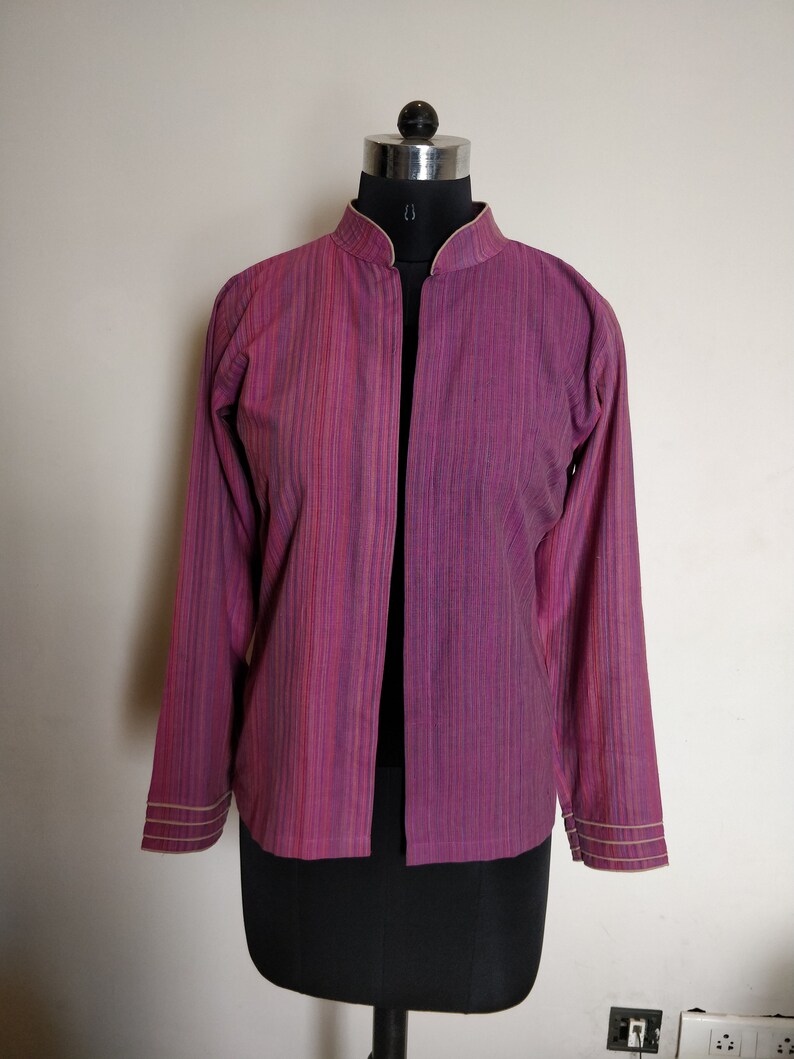 Puede incluir: Una chaqueta de manga larga, abierta por delante, con cuello mandar&iacute;n. La chaqueta est&aacute; hecha de una tela a rayas en tonos rosa, morado y blanco. Los pu&ntilde;os y el cuello est&aacute;n ribeteados con una fina tela de color crema.