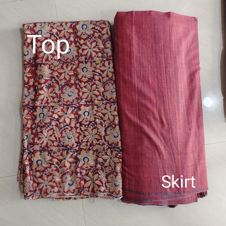 Puede incluir: Un conjunto de tela de dos piezas con una parte superior y una falda. La parte superior tiene un fondo rojo con un estampado floral en crema, amarillo y azul. La falda es de color rojo liso, con la palabra "Skirt" impresa.