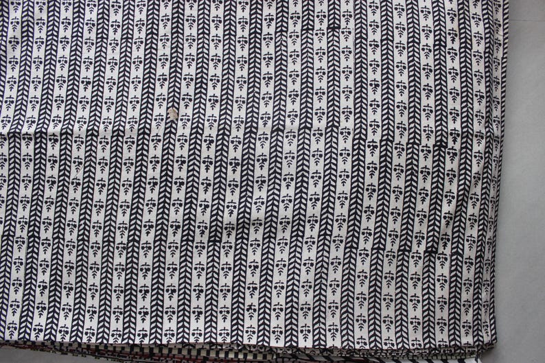 May include: A textile fabric featuring a repeating pattern of vertical black stripes alternating with rows of small black floral motifs on a white background. The design consists of a herringbone-style chevron stripe next to a column of stylized flowers.