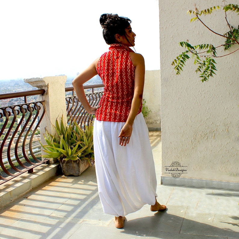 May include: A sleeveless red top featuring a white repeating wave pattern and a high collar, paired with loose-fitting white trousers. The top has a button-down front and a fitted silhouette, while the trousers have a wide-leg, flowing design.