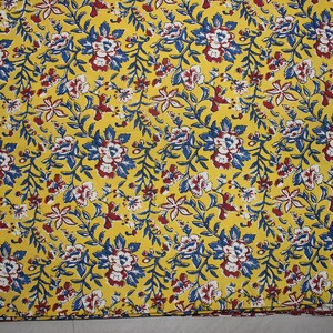 May include: A vibrant yellow fabric featuring a dense, repeating floral pattern. The design consists of small white flowers with dark red centers, interspersed with blue leaves and thin, winding stems that cover the entire surface of the textile.