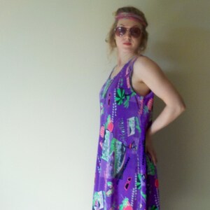 May include: A woman wearing a purple sleeveless dress with a colorful print. She is wearing a headband and sunglasses.