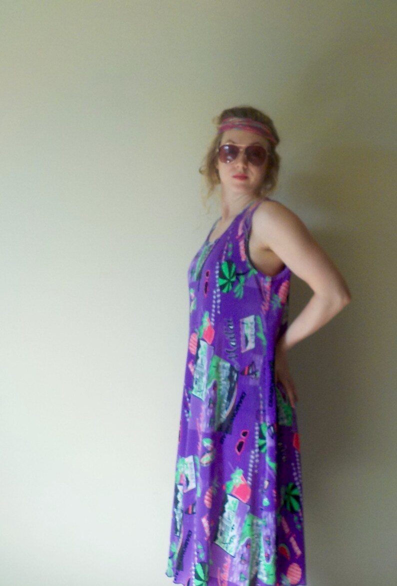 May include: A woman wearing a purple sleeveless dress with a colorful print. She is wearing a headband and sunglasses.