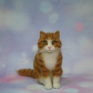 May include: A needle-felted orange and white tabby cat figurine with yellow eyes, a pink nose, and long, thin, clear whiskers. The cat is in a seated position, featuring textured orange fur stripes on its head and back, with a solid white chest and paws.