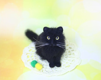 May include: A black cat with white whiskers sits on a white crocheted doily with green and yellow yarn balls.
