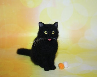 May include: A black cat ornament with yellow eyes and a pink tongue. The cat is posed sitting with its tail curved. Two small, round, orange and white pom-poms are in front of the cat against a yellow backdrop.