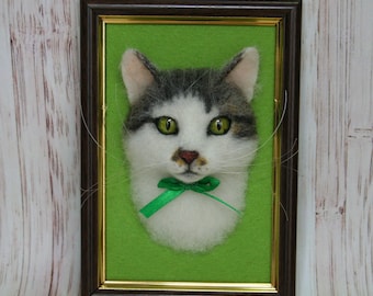 May include: A framed felt art piece featuring a cat's face. The cat has white and gray fur, green eyes, and a green ribbon bow. The artwork is set against a green background within a brown frame.