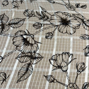 Pode incluir: Um tecido branco com um padrão xadrez branco e preto e um desenho floral preto. As flores são rosas estilizadas com folhas e caules.