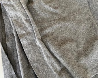 Może przedstawiać: Zbliżenie złożonej, jasnoszarej tkaniny. Materiał ma miękki, teksturowany wygląd. Widoczne są krawędzie tkaniny, pokazujące surową, niewykończoną krawędź. Tkanina wydaje się być materiałem o średniej gramaturze.