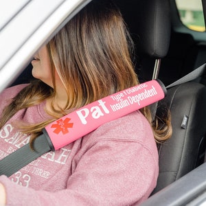 May include: Pink car seatbelt cover with a white star of life and the text "Pat Type 1 Diabetic Insulin Dependent".