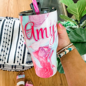 May include: A pink and blue marble patterned tumbler with a black lid and a pink and white striped straw. The tumbler has the name "Amy" written on it in white letters.