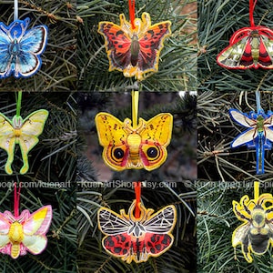May include: Nine colorful felt ornaments featuring different insects, including butterflies, moths, and a dragonfly. The ornaments are hanging on a green pine tree branch.