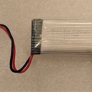 May include: A white lithium polymer battery with black wires and a white connector. The battery has the text "Busy Bee Digital 903045 3.7V 1500mAh 20220214" printed on it.