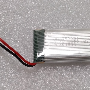 May include: A silver lithium polymer battery with black and red wires. The battery has the text "JH 352051 3.7V 1100mAh 1S" and "20201015" printed on it.