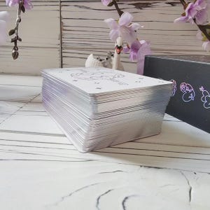 May include: A stack of white playing cards with a black and white illustration of a swan on the top card. The cards are on a white wooden surface.