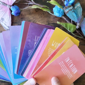 K&ouml;nnte beinhalten: Ein Satz farbenfroher Affirmationskarten mit Aquarellhintergr&uuml;nden. Die Karten zeigen positive Botschaften wie "Lebe deine Wahrheit" und "Intention".