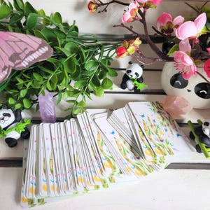 May include: A deck of cards with a white background and a green bamboo design. The cards are stacked and fanned out, showing the design on each card. There are small panda figurines and a pink butterfly on the table.