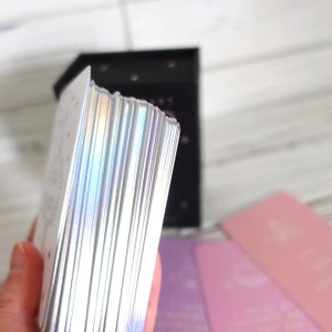 May include: A stack of iridescent white cards with rounded corners. The cards are in a black box with a silver lid.