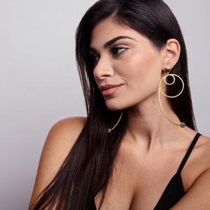 Model wearing long geometric gold statement earrings with circular design, modern sculptural dangle earrings in gold plated brass, fashion forward minimalist jewelry.