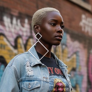 May include: A light blue distressed denim jacket worn over a black cropped t-shirt with a graphic print and black cargo pants. Large geometric diamond-shaped silver earrings are visible. The t-shirt features a circular graphic with red and yellow tones.