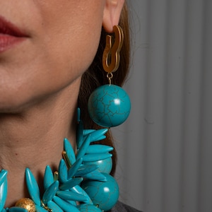 Peut inclure: Un collier et des boucles d'oreilles imposants de couleur turquoise et or. Le collier présente une grande sphère turquoise, des sphères turquoise plus petites et des pointes turquoise. Les boucles d'oreilles présentent une sphère turquoise et une boucle dorée.