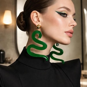 May include: A pair of large, glossy, dark green snake-shaped earrings with a smooth, curved, serpentine silhouette. Each earring features a gold-toned metal stud attachment at the top, securing the dangling, abstract, wavy green form to the earlobe.