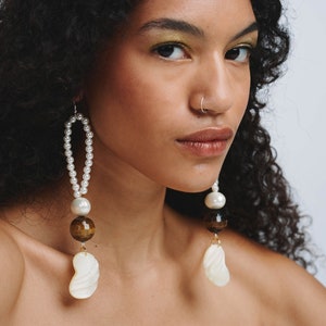 May include: A pair of long, dangling earrings with white pearls, brown tiger's eye beads, and white shell accents.
