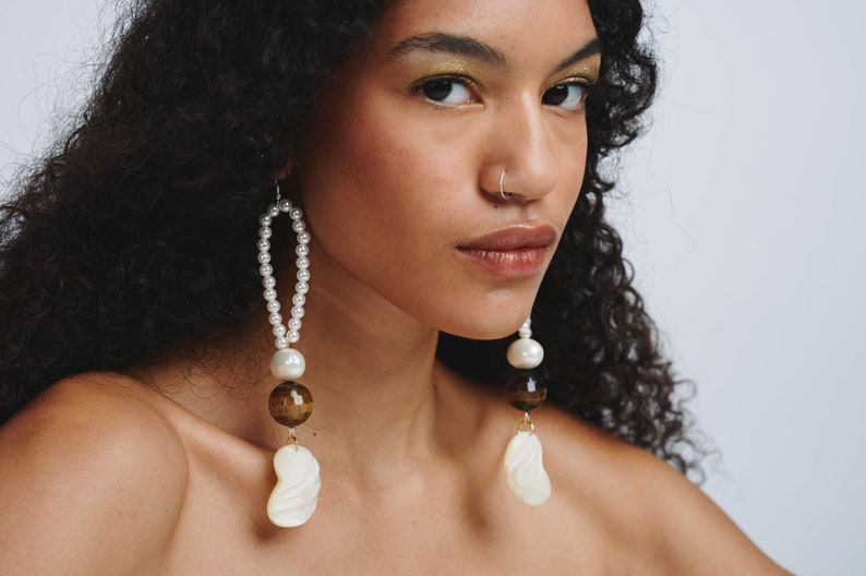 May include: A pair of long, dangling earrings with white pearls, brown tiger's eye beads, and white shell accents.