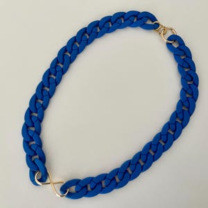 May include: A blue rubber chain necklace with gold clasps. The chain is thick and chunky, and the clasps are simple and elegant.