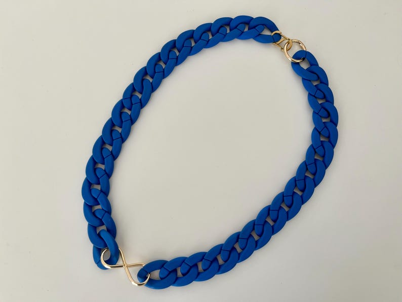 May include: A blue rubber chain necklace with gold clasps. The chain is thick and chunky, and the clasps are simple and elegant.