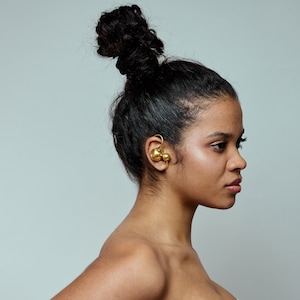 May include: A woman with dark hair styled in a high bun wears a gold ear cuff with two round, gold spheres.