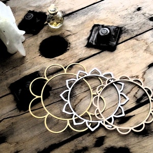 May include: Three decorative metal hoops with a floral design. The hoops are gold and silver and are arranged in a circle on a wooden surface.