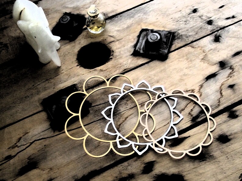 May include: Three decorative metal hoops with a floral design. The hoops are gold and silver and are arranged in a circle on a wooden surface.