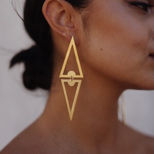 May include: A pair of gold geometric earrings with a triangle shape. The earrings are long and dangle from the earlobe.