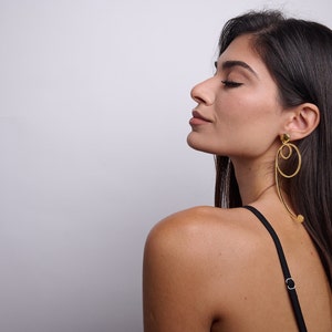 May include: A woman with long dark hair wearing a black tank top and gold hoop earrings with a dangling circle design.