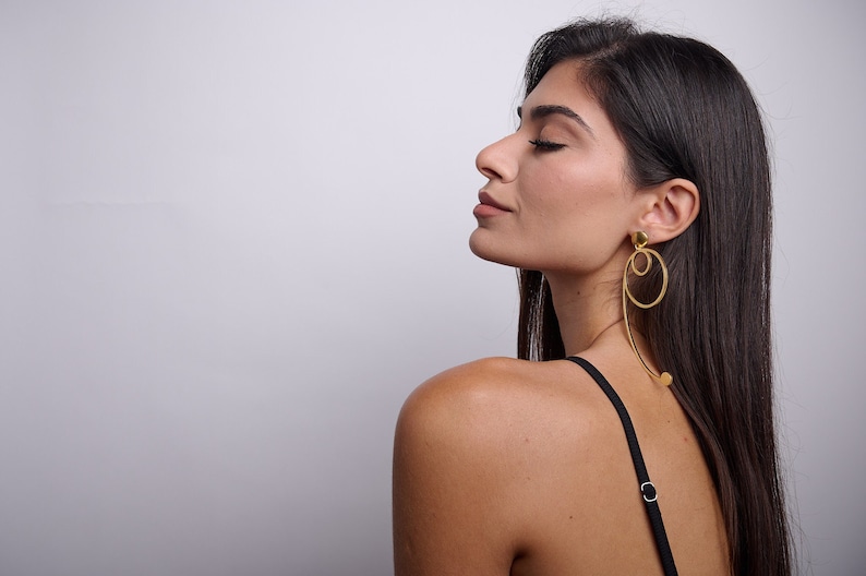 May include: A woman with long dark hair wearing a black tank top and gold hoop earrings with a dangling circle design.