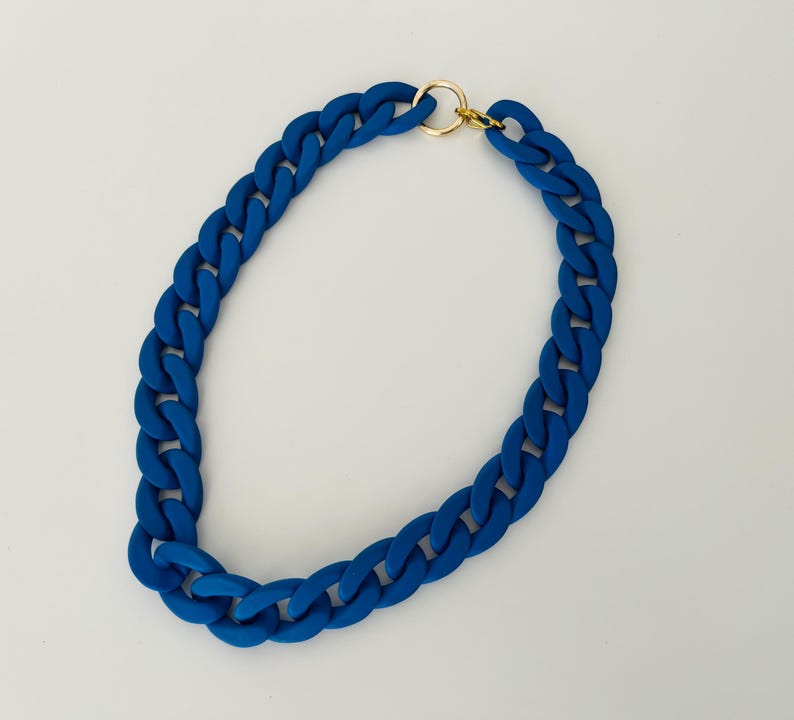 May include: A thick, blue chain necklace with a gold clasp. The chain is made of a chunky, rubber-like material.